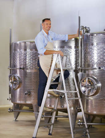 Double checking is key. Portrait of a mature wine maker standing next to his steel vats in his...