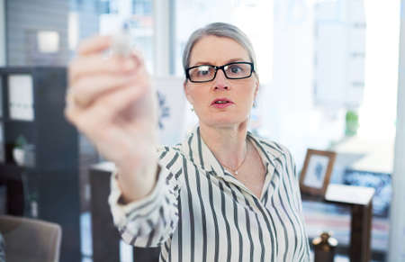 She has a vision and shes going to make it work. Shot of a mature businesswoman writing notes on a glass wall in an office.の写真素材