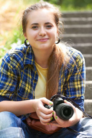 Thinking about starting her own business in photography. A gorgeous young woman sitting on the stairs in her garden holding her camera.の写真素材