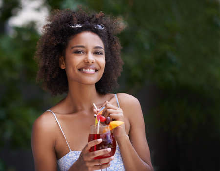 Cocktails and sunshine make me a happy lady. Shot of an attractive young woman enjoying a cocktail...