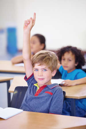 Hell answer your question. Portrait of a young boy holding his hand up in class to answer a question.の写真素材