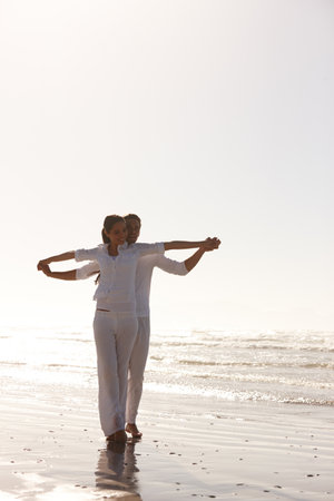 Revelling in the mornings light. Full length shot of an attractive young couple dressed in white walking along a beach.の写真素材