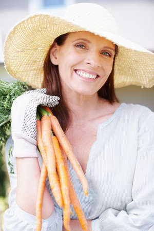 A bunch of goodness. Portrait of a smiling woman holding up a bunch of carrots.の写真素材