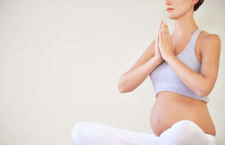 Keeping her mind and body in good shape for the baby. A young pregnant woman sitting in a yoga pose - cropped.の写真素材