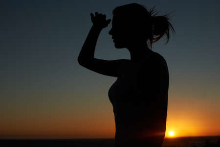 As far as the eye can see. Silhouette of a young woman looking into the distance against a setting sun.の写真素材