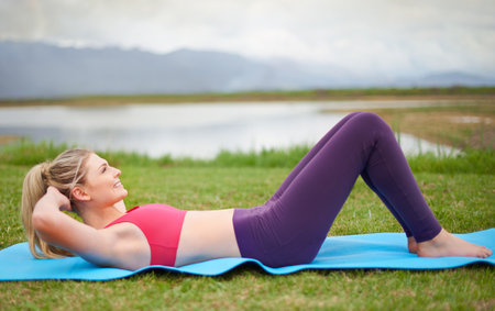 Keeping her core muscles strong. Shot of a young woman doing sit-ups in the outdoors.の写真素材
