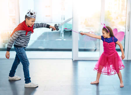 The battle of good vs evil. Full length shit of two young children dressed up as superheroes play fighting at home.の写真素材