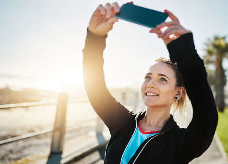 I deserve a selfie after that run. Cropped shot of a woman taking a selfie while out for a run on the promenade.の写真素材