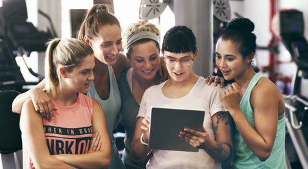 Showing them her fitness app. Cropped shot of a group of young women looking at a digital tablet in...