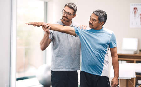 It all starts with a stretch. Shot of a senior man going through rehabilitation with his physiotherapist.の写真素材