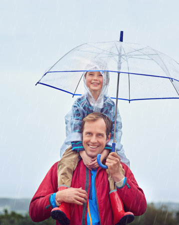 The weather wont stand in our way. Cropped portrait of a father carrying his son on his shoulders outside in the rain.の写真素材