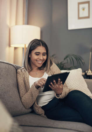 Turning her tablet into a mini tv. Shot of a young woman using a digital tablet on the sofa at home.の写真素材