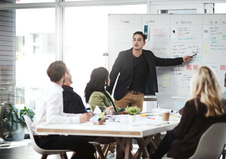 This is how we will execute our latest strategy. Shot of a businessman giving a presentation to his colleagues on a whiteboard in a boardroom.の写真素材