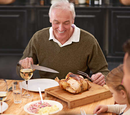 Chicken for lunch. Shot of a senior man enjoying some roast chicken at the dinner table.の写真素材