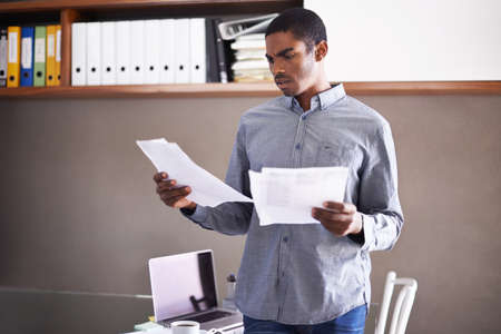 Going over the details of the contract. Shot of a handsome young businessman looking over some paperwork in his home office.の写真素材