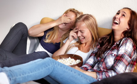 This is hilarious. Shot of three young friends enjoying a bowl of popcorn while watching a movie.の写真素材