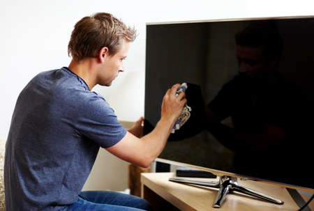 Taking care of his electronics. Young man cleaning the screen of his smart TV.の写真素材
