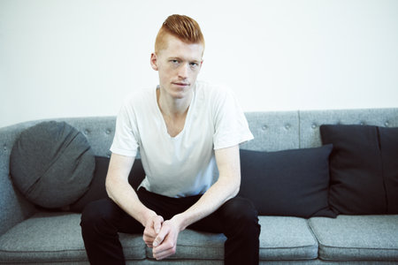 The serious type. A caucasian ginger sitting on a couch looking at the camera.