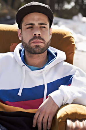 A tough guy in a tough neighborhood. Portrait of a serious man sitting on a couch in the outdoors.