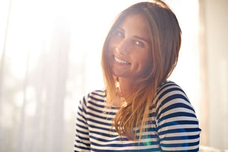 Bathed in morning light. Cropped shot of a beautiful young woman bathed in window light.の写真素材