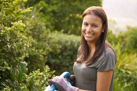 Surrounded by natures beauty. Shot of an attractive young woman watering her garden.