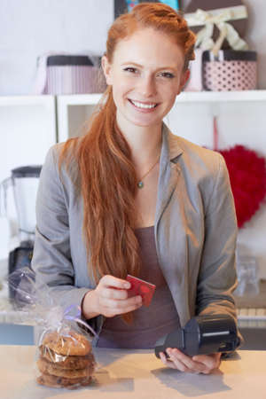 Thank you, please come again.... Portrait of an attractive young woman swiping your card in her bakery.の写真素材