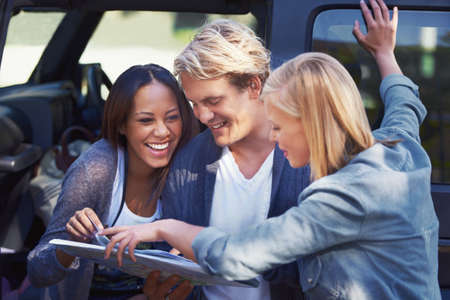 Lets get lost for fun. Portrait of a group of friends leaning against their van, reading a map.の写真素材