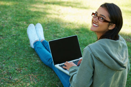 Connected - anywhere, anytime. A young woman working on her laptop in the park.の写真素材