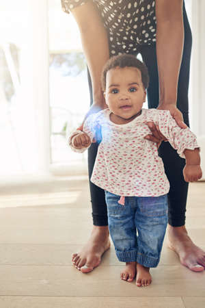 Baby steps. Portrait of a smiling baby girl standing with the support of her mother.