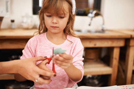 Moms always there to lend a hand. Shot of a little girl being helped with scissors.の写真素材