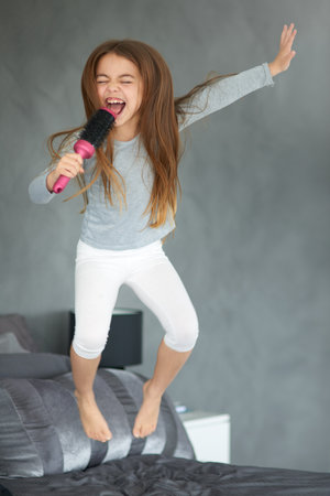 This one goes out to my fans. Shot of a cute little girl jumping on a bed while pretending to sing into a hairbrush.の写真素材