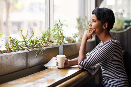 Coffee shop contemplation. An attractive young woman looking thoughtful while having coffee at a...