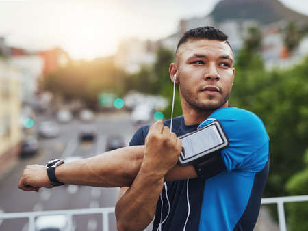 Getting ready for some action. Shot of a young man stretching before a run in the city.