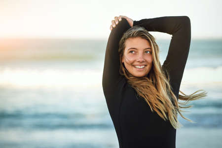 Youve gotta be limber to be a surfer. Cropped shot of an attractive young female surfer warming up on the beach.の写真素材