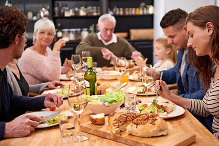Drink, eat and be merry. Cropped shot of a family sharing a meal around the dinner table.の写真素材