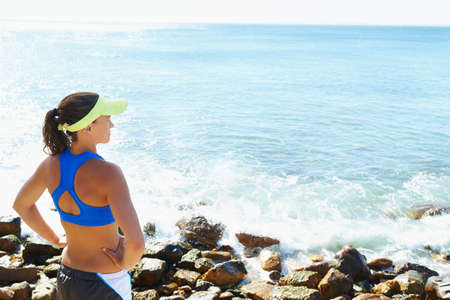 What a wonderous view. Rearview shot of a young woman looking out over the sea with her hands on her...
