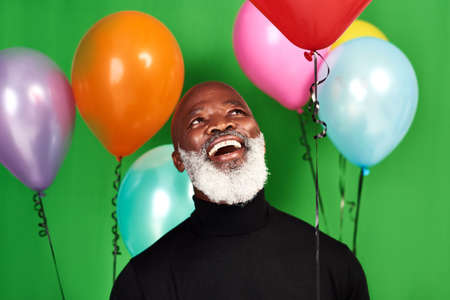 Live your life and be merry. Studio shot of a man posing against a green background with balloons around him.の写真素材