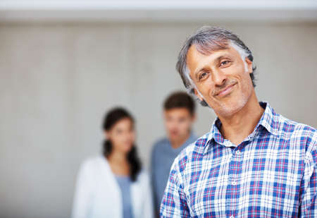 Mature architect with couple in background. Portrait of mature architect smiling with couple in...