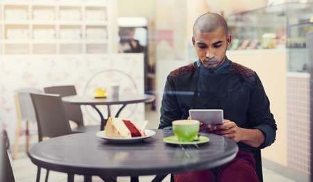 I come for the coffee but mostly for free wifi. Shot of a young man sitting in a cafe with his...