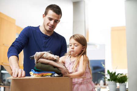Daddys little helper. A father and daughter packing clothes in a donations box.の写真素材