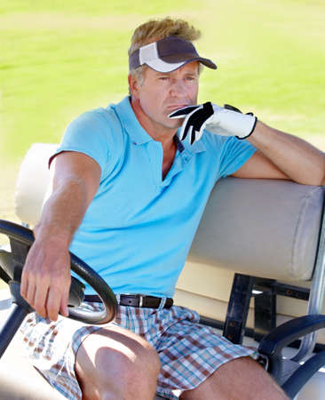 Planning his next shot. A mature man sitting in a golf cart looking thoughtfully into the distance.の写真素材