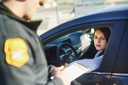 You were going way over the speed limit. Cropped shot of an unrecognizable male traffic officer issuing a ticket to a female civilian at a roadblock.の写真素材