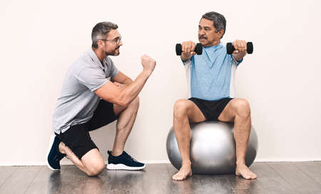 Balance is key in everything in life. Full length shot of a senior man exercising with dumbbells during a rehabilitation session with his physiotherapist.の写真素材