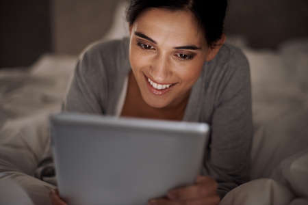 Chatting with him late into the night. Cropped shot of an attractive young woman using her tablet in...