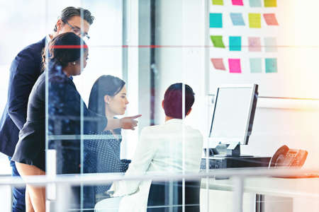 Taking a closer look. Cropped shot of four business colleagues working in the office.の写真素材