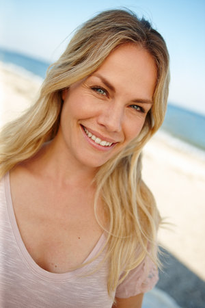 The perfect spot to get away from it all. Head and shoulders portrait of an attractive young woman standing on a sunny beach.の写真素材