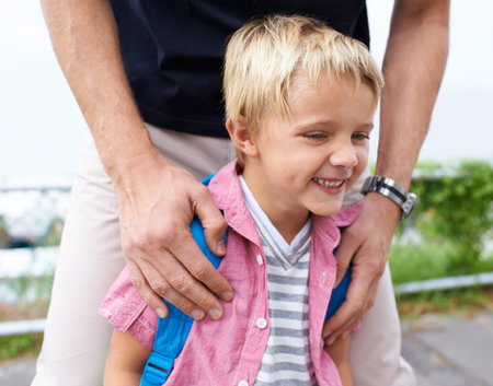 My dad always has my back. A little boy smiling outside with his dad standing behind him.