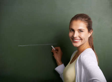 Shaping the future generation. A beautiful young teacher writing on a blackboard while smiling at...