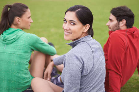 Friends and fitness. Portrait of young people in exercise clothing sitting on a grassy sports field.の写真素材