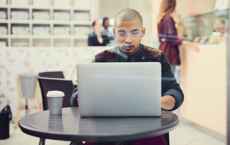 Enjoying some online time at his favourite cafe. Shot of a young man using his laptop in a coffee shop.の写真素材